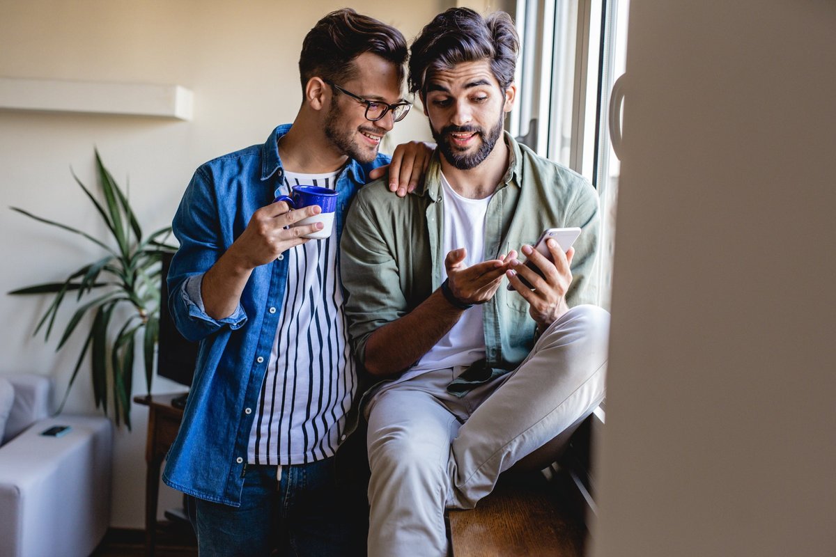 Two people sitting in a window at home and looking at the phone in one of their hands.