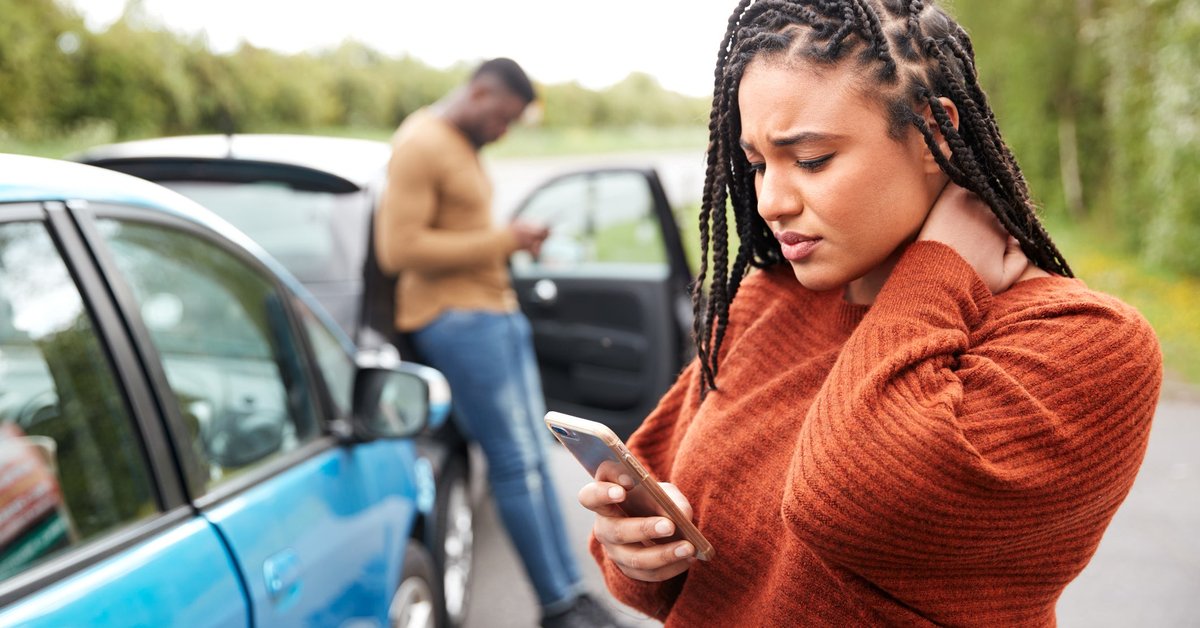 Two people standing next to their cars and looking at their phones after being in a minor car accident.