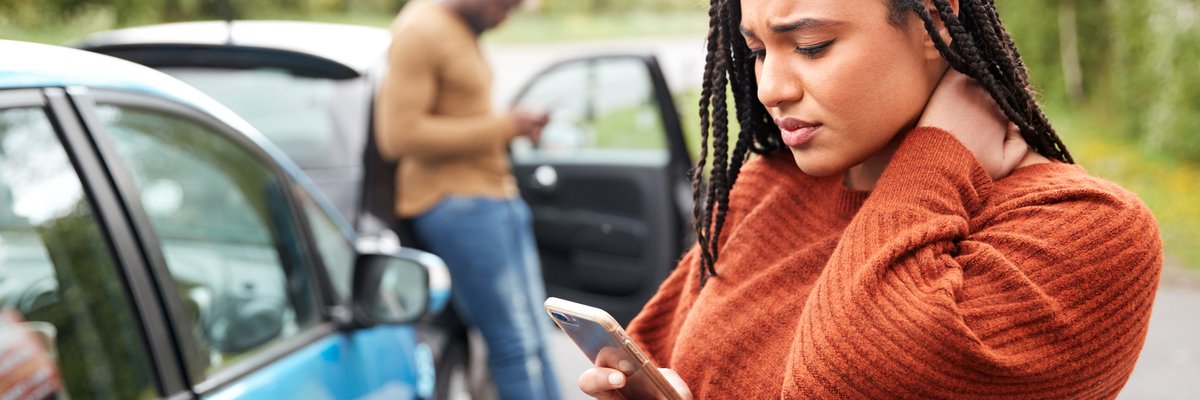 Two people standing next to their cars and looking at their phones after being in a minor car accident.