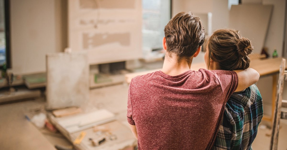 Two people with their arms around each other looking at their living room under construction.