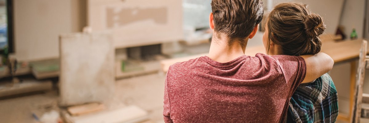 Two people with their arms around each other looking at their living room under construction.