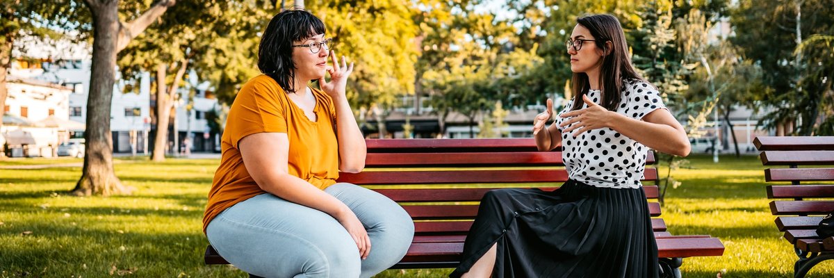 Two people sitting on a park bench and speaking in sign language.