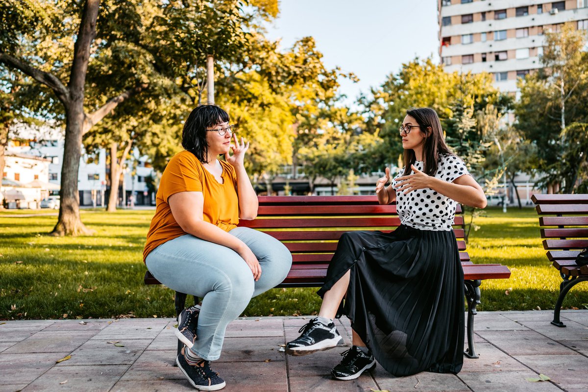 Two people sitting on a park bench and speaking in sign language.