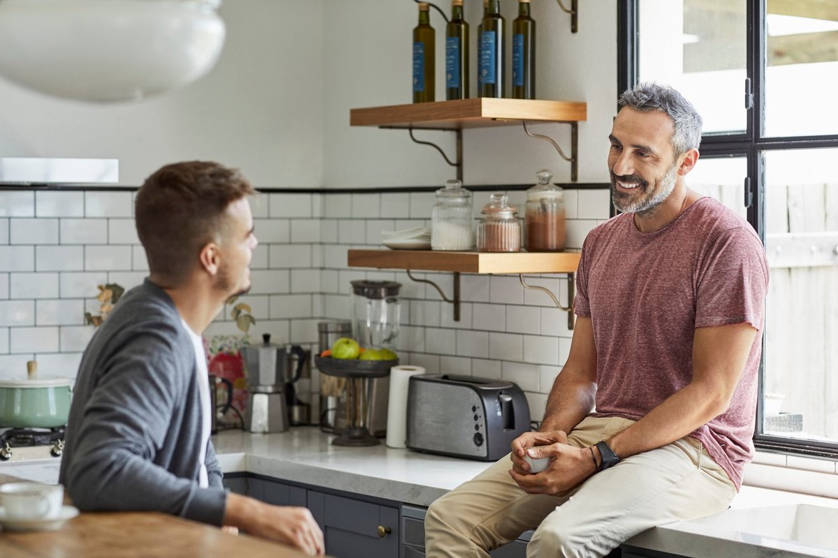 Two people sitting on their kitchen counter and talking.