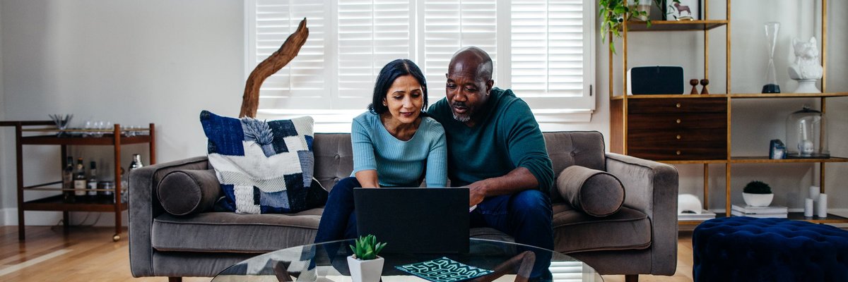 Two people sitting on a couch in their living room while typing on a laptop on the coffee table.