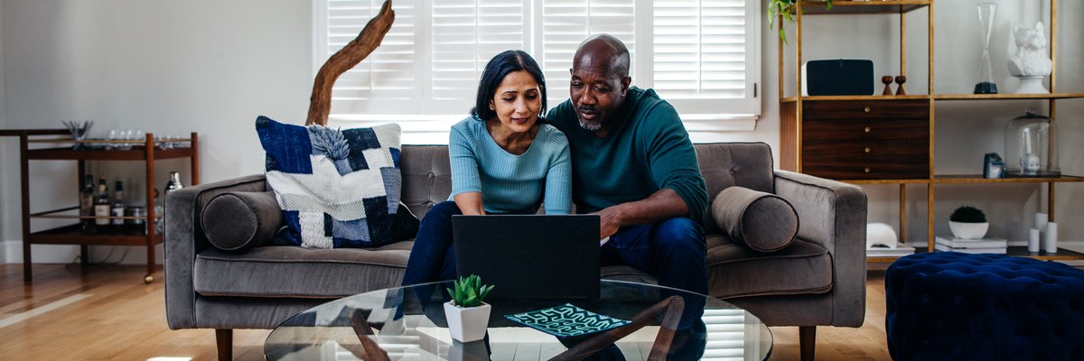 Two people sitting on a couch in their living room while typing on a laptop on the coffee table.
