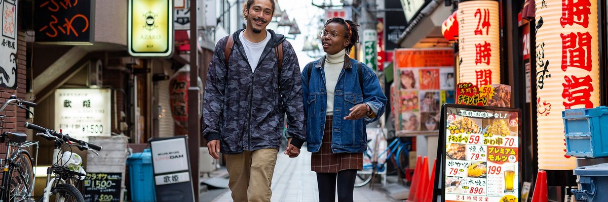 Two smiling people holding hands and walking down a small side street in Tokyo, Japan.