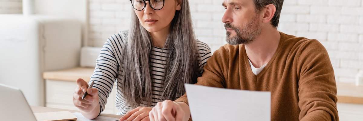 Two people sitting at their kitchen table with an open laptop, paperwork, and a calculator.