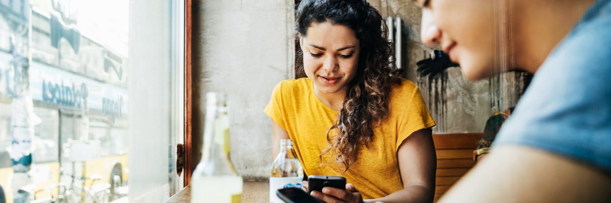Two people sitting at a window table in a restaurant and looking at their cellphones.