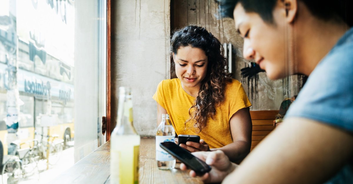 Two people sitting at a window table in a restaurant and looking at their cellphones.