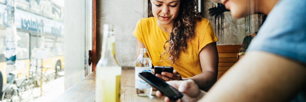 Two people sitting at a window table in a restaurant and looking at their cellphones.