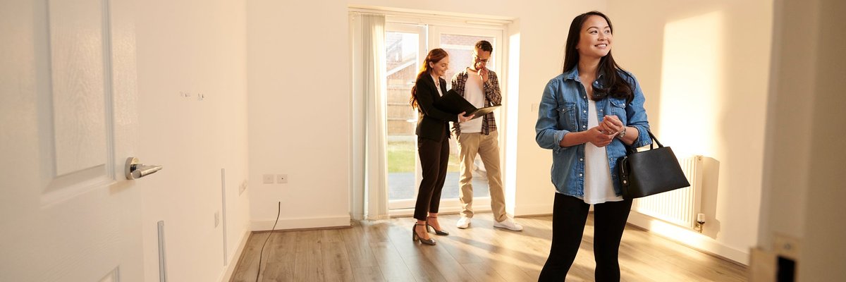Two people walking through an empty room in a house with a realtor.