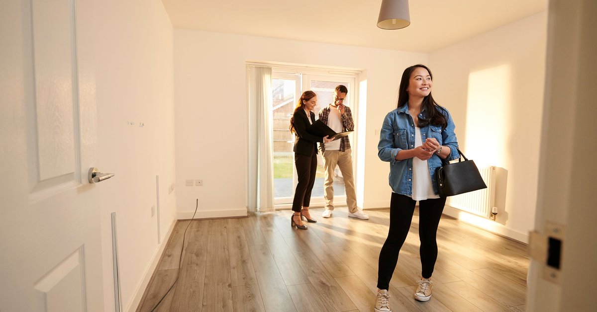 Two people walking through an empty room in a house with a realtor.