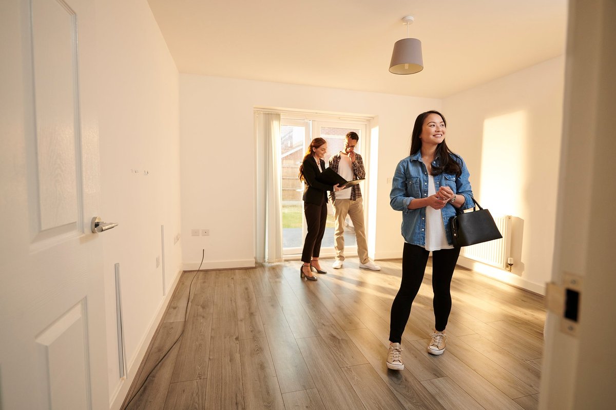 Two people walking through an empty room in a house with a realtor.