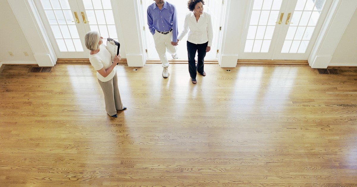 Two people walking into an empty house with their realtor.