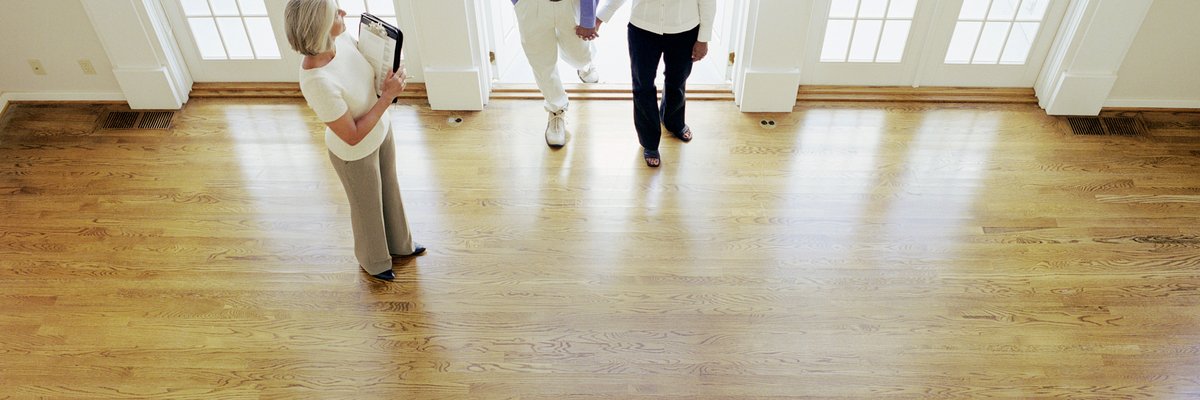 Two people walking into an empty house with their realtor.