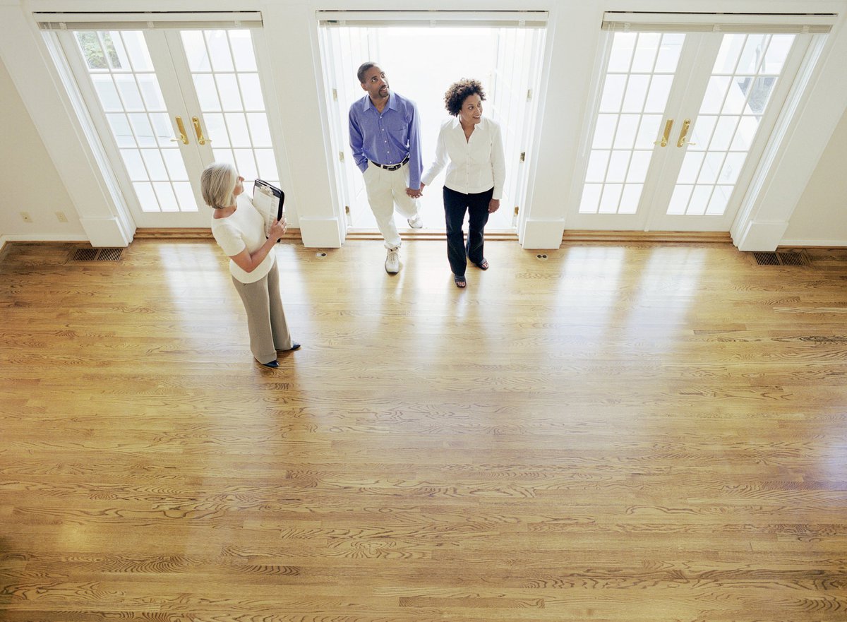 Two people walking into an empty house with their realtor.