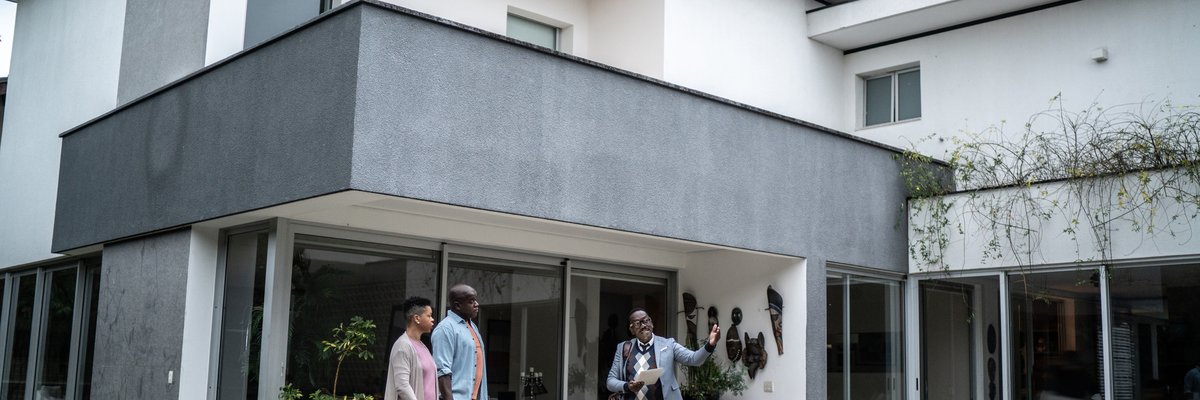 Two people speaking with a real estate agent while looking at a pool in the backyard of a house.
