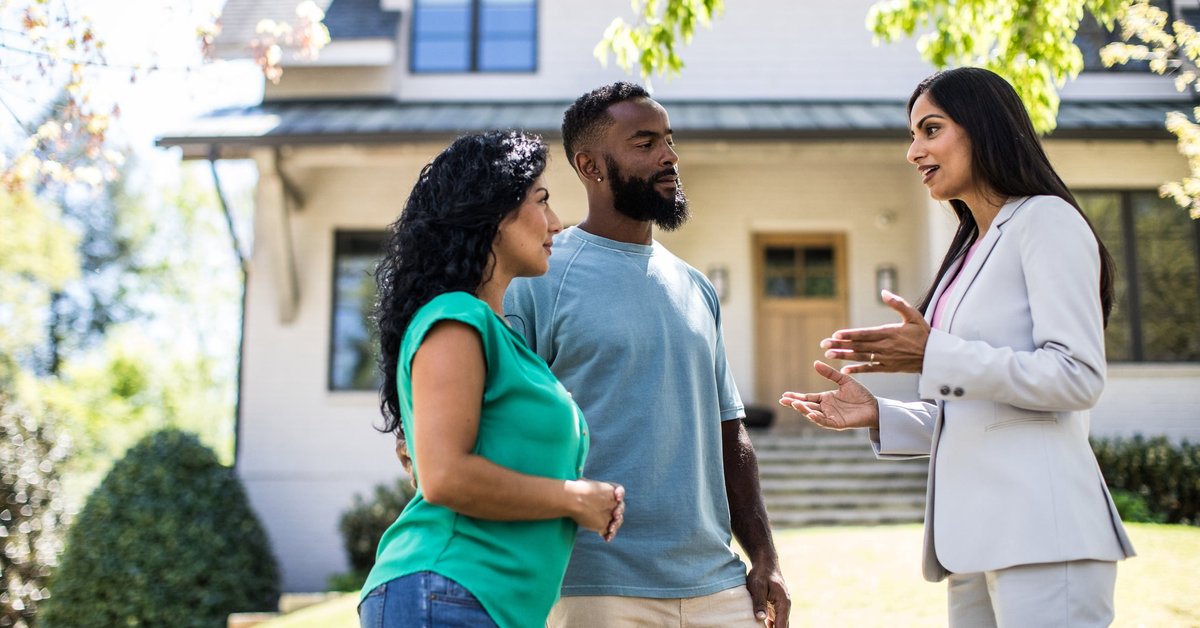 Two people standing in the front yard of a house and speaking with their realtor.