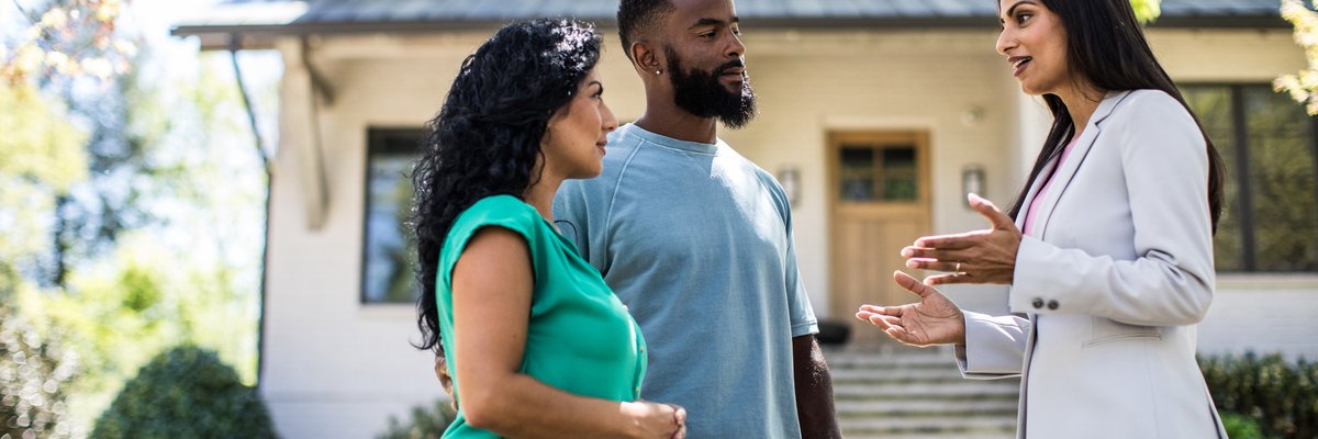 Two people standing in the front yard of a house and speaking with their realtor.