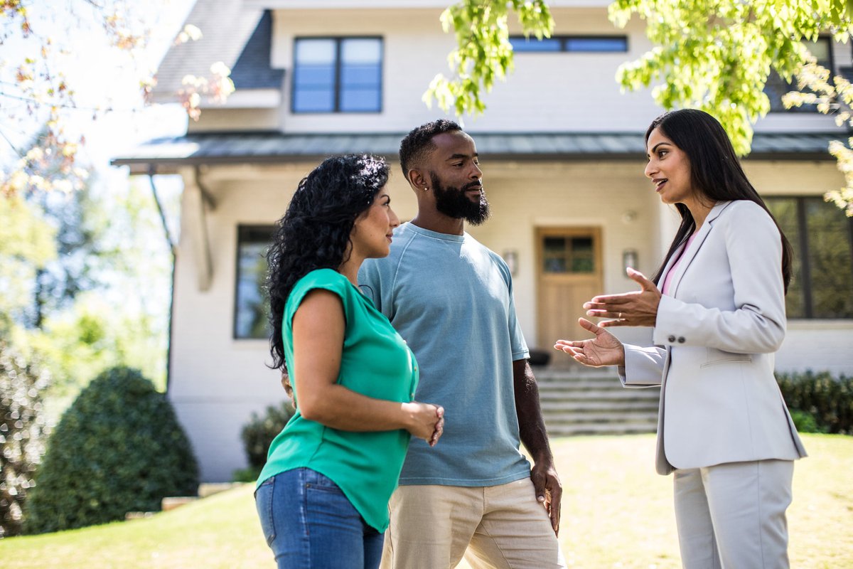 Two people standing in the front yard of a house and speaking with their realtor.