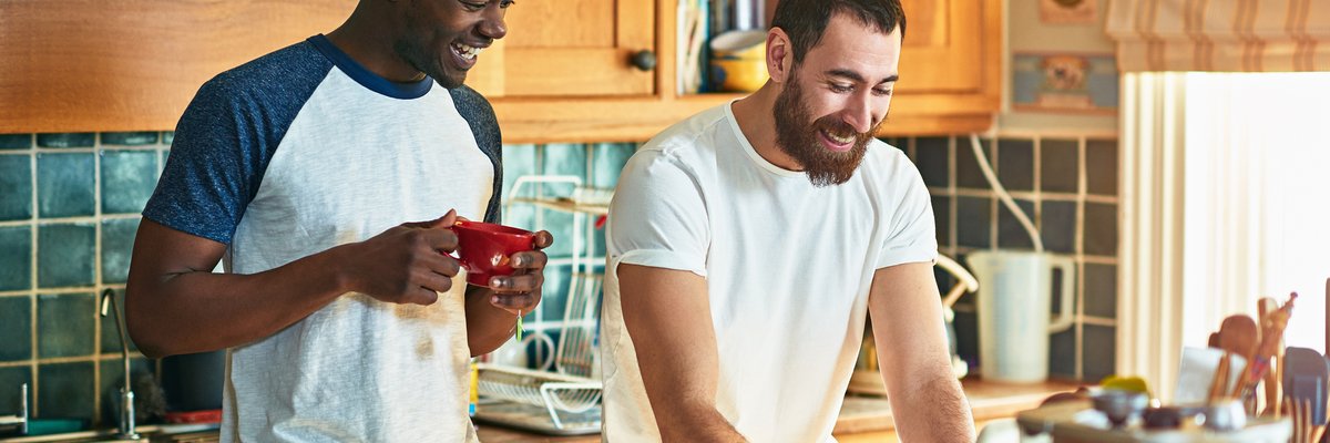 Two roommates laughing while watching something on a computer on the kitchen counter.