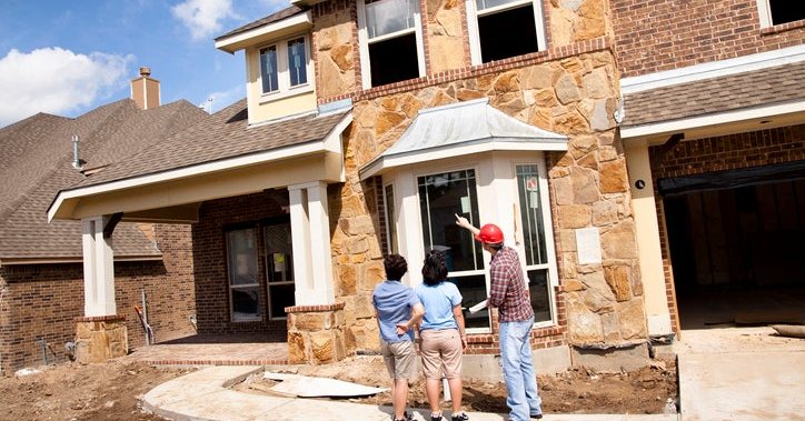 Two women speaking with the builder in front of a partially constructed home.