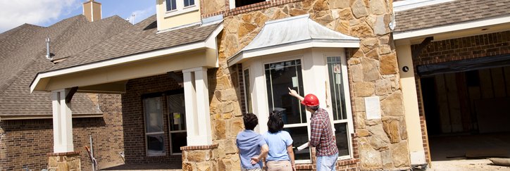 Two women speaking with the builder in front of a partially constructed home.