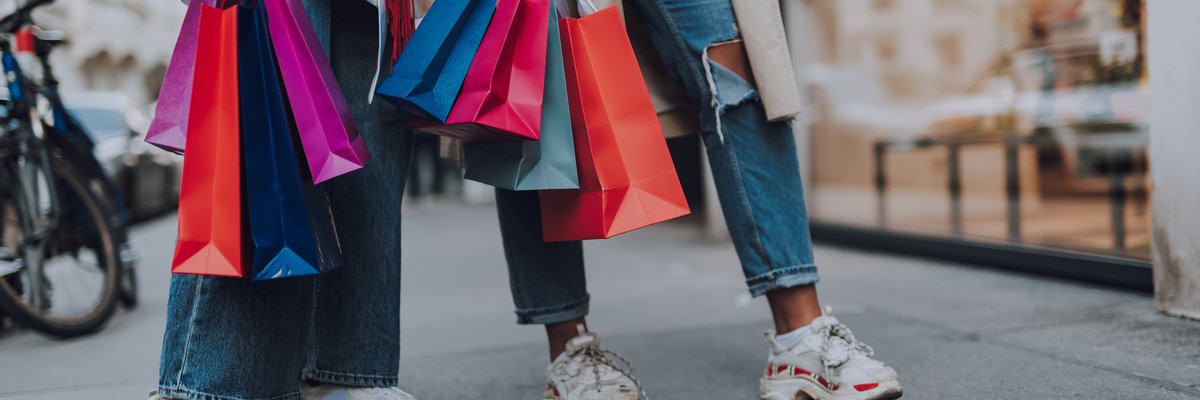 Two women holding lots of shopping bags while standing outside a storefront on the street.