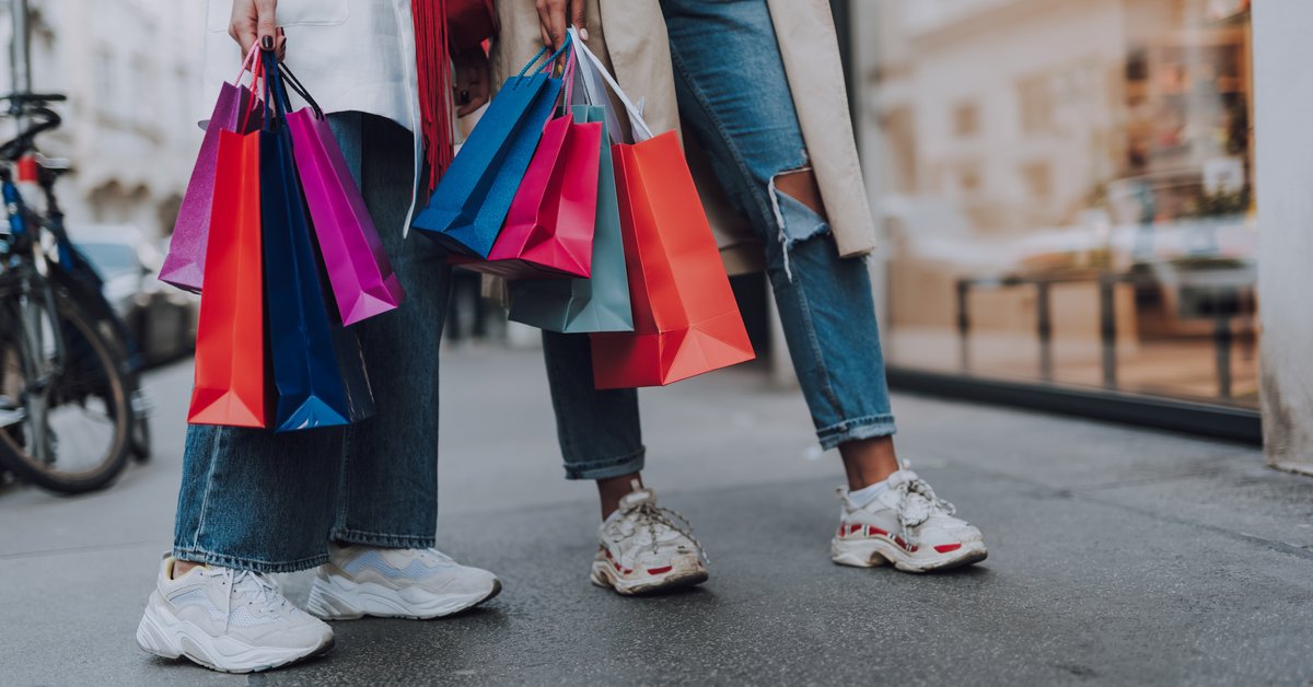 Two women holding lots of shopping bags while standing outside a storefront on the street.
