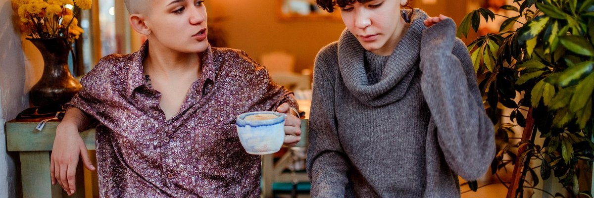 Two women sitting in a cafe while one looks at a tablet in her lap.