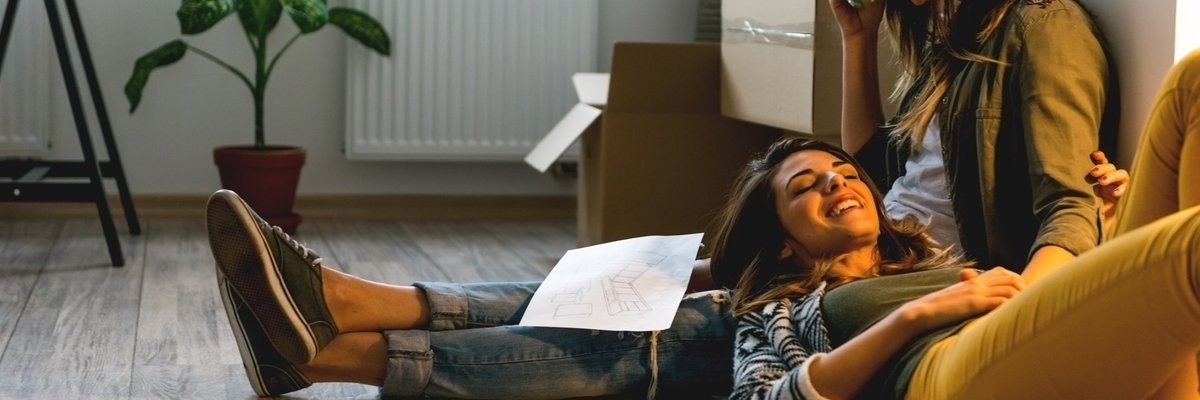 A woman lying on the floor with her head resting on her girlfriend's lap.