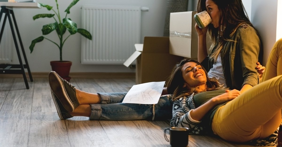 A woman lying on the floor with her head resting on her girlfriend's lap.