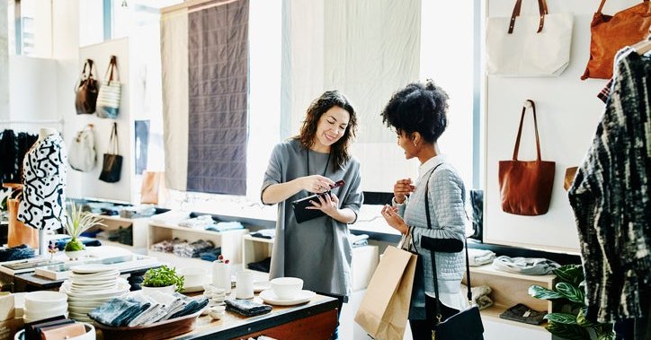 A woman swiping another woman's credit card in a payment reader while standing in a local clothing store.