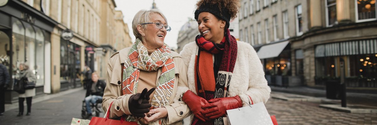 Two women walking down a street arm in arm carrying shopping bags.