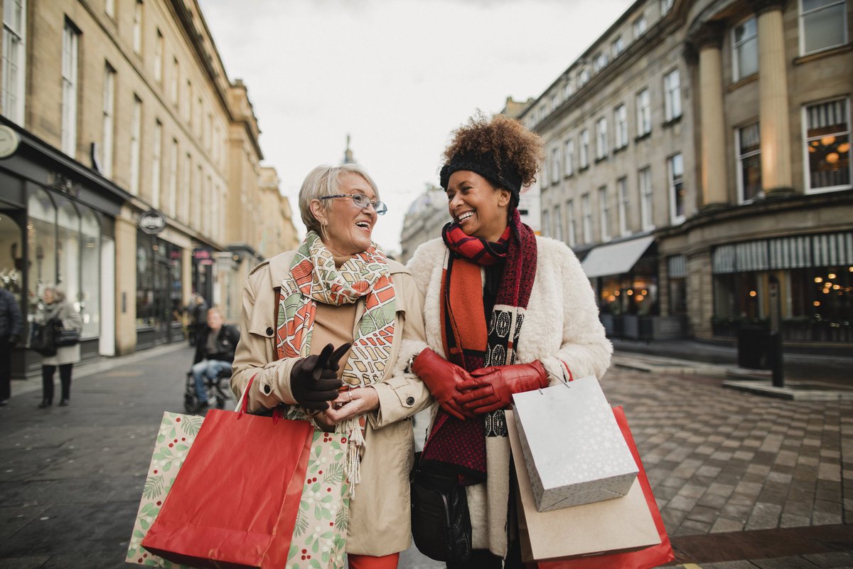 Two women walking down a street arm in arm carrying shopping bags.
