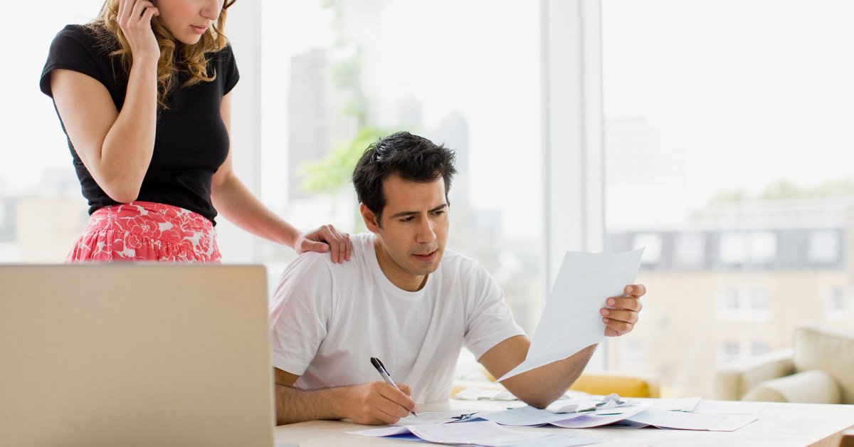 Two people looking worried while reviewing bills at their kitchen table.