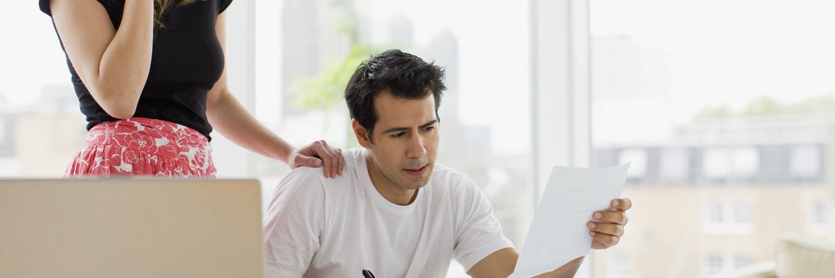 Two people looking worried while reviewing bills at their kitchen table.