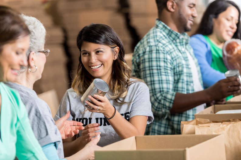 A group of smiling volunteers packing canned food in boxes.