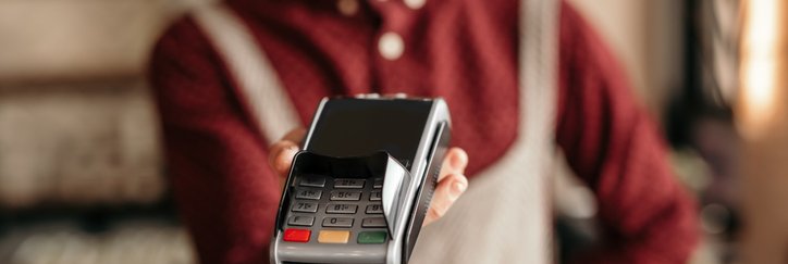 A waiter wearing an apron and holding up a credit card reader awaiting payment.
