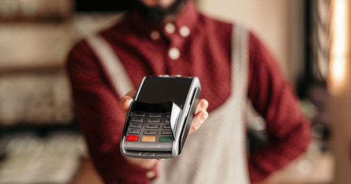 A waiter wearing an apron and holding up a credit card reader awaiting payment.