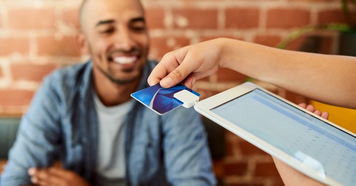 A person looking on as a waiter swipes a credit card in a payment tablet.