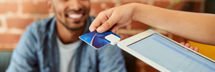 A person looking on as a waiter swipes a credit card in a payment tablet.