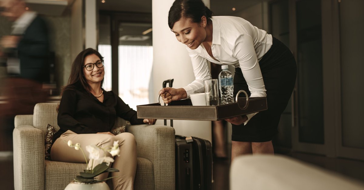 A waitress bringing a tray of drinks to a customer in an airport lounge.