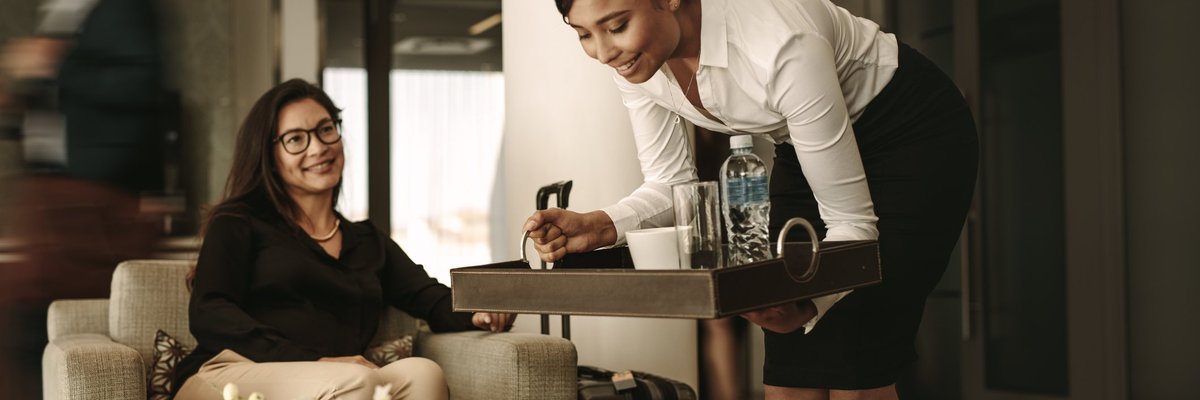 A waitress bringing a tray of drinks to a customer in an airport lounge.
