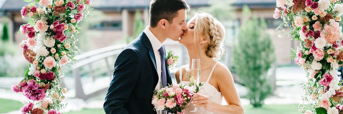 Bride and groom kissing under floral canopy