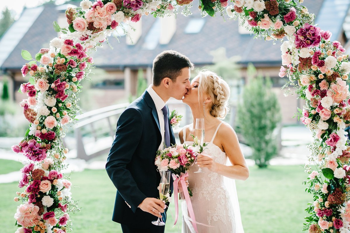 Bride and groom kissing under floral canopy