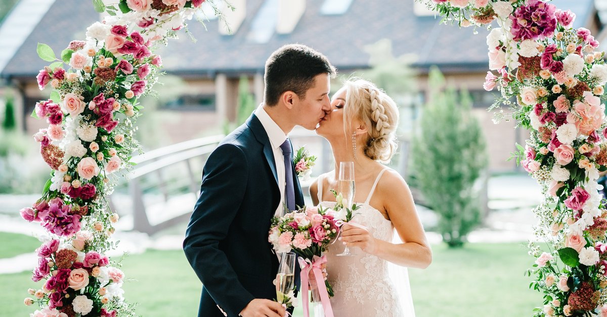Bride and groom kissing under floral canopy