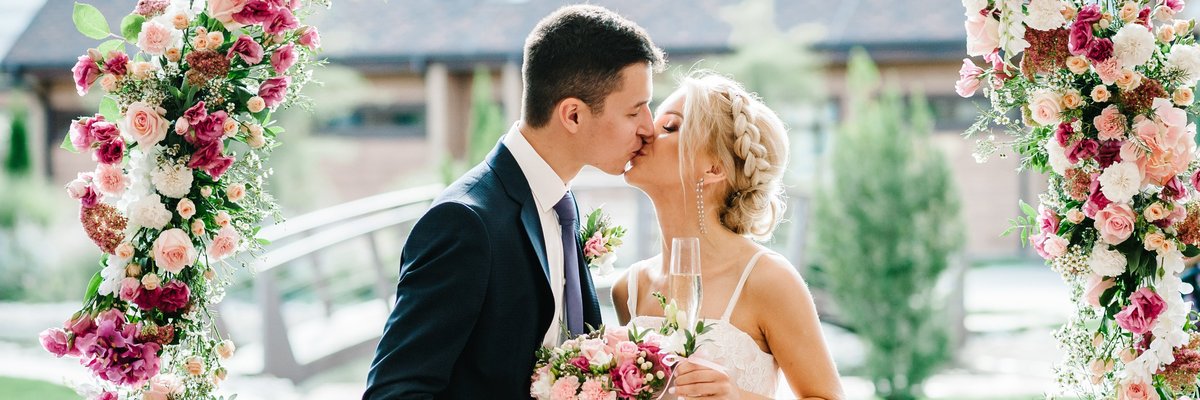 A bride and groom kissing underneath a flower arch.