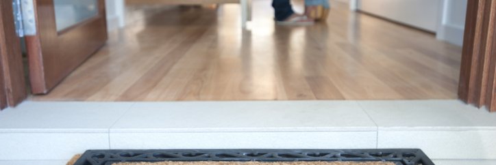 A welcome mat at the open front door of a new house with a man and woman standing inside.